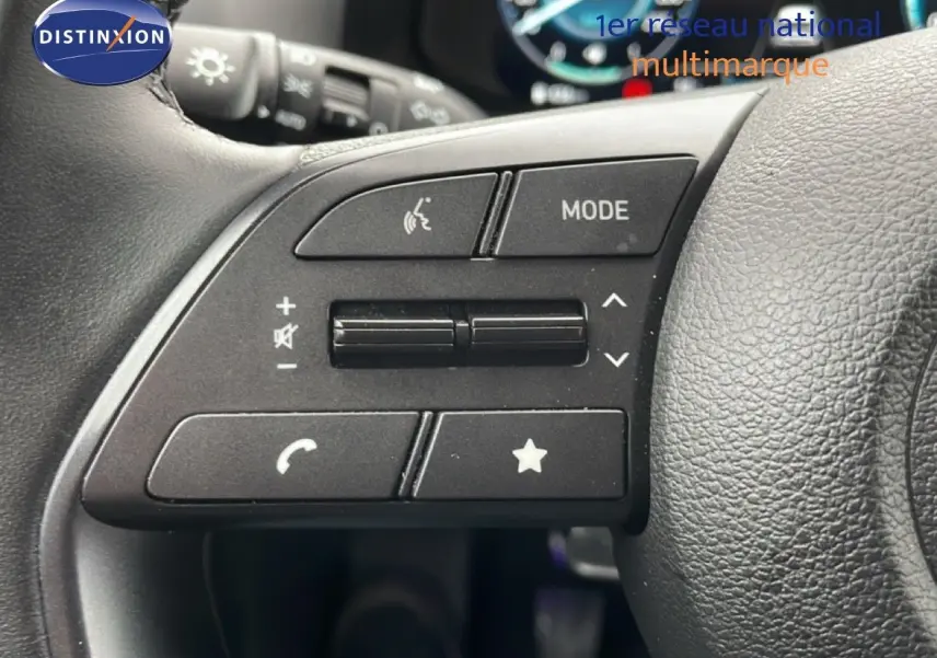 Gros plan sur les commandes au volant côté gauche d'une Hyundai i20 2025 vert mangrove métal, avec boutons multifonctions.