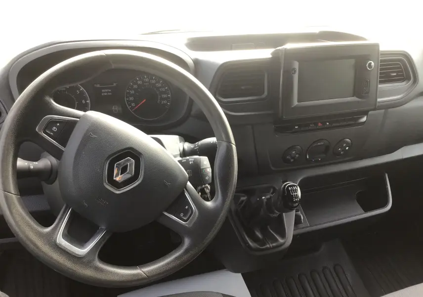 Vue intérieure du poste de conduite du Renault Master blanc, avec volant, tableau de bord et levier de vitesses manuel visibles.