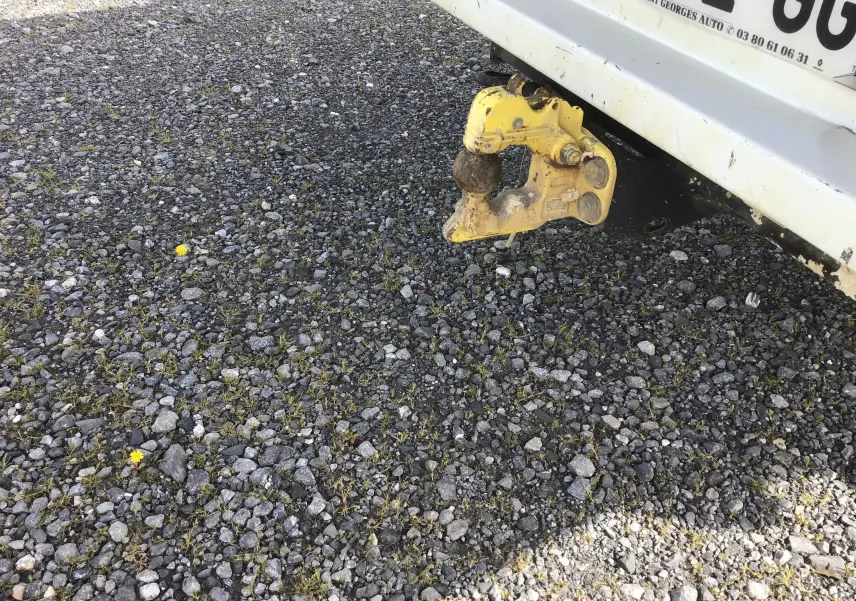 Vue rapprochée de l'arrière blanc d'un Renault Master avec attelage jaune sur un sol gravillonné.
