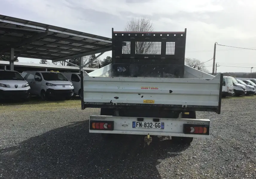Vue arrière d'un Renault Master blanc avec benne et grille de protection noire, stationné sur un sol gravillonné.