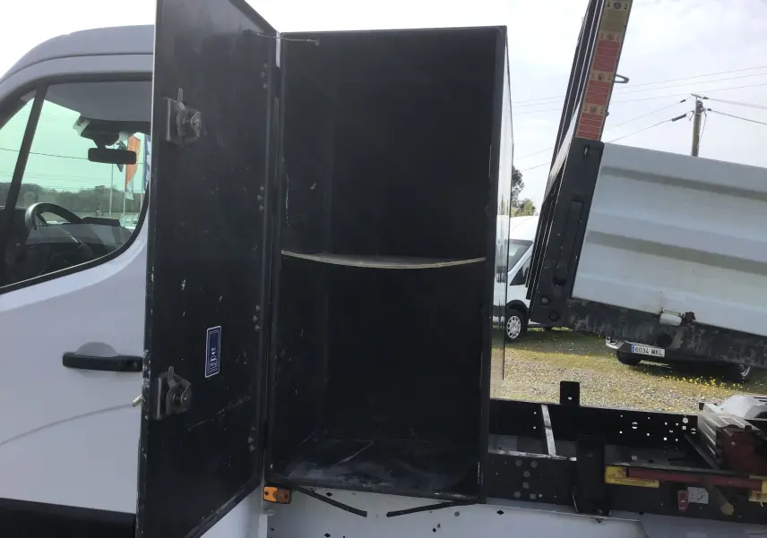 Vue latérale gauche d’un Renault Master blanc avec coffre ouvert et benne relevée, montrant la structure et le rangement arrière.