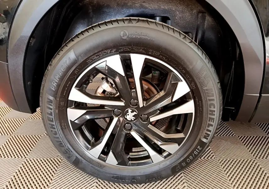 Gros plan sur la roue avant droite noire et argentée d’un Peugeot 2008 noir, avec logo lion au centre.