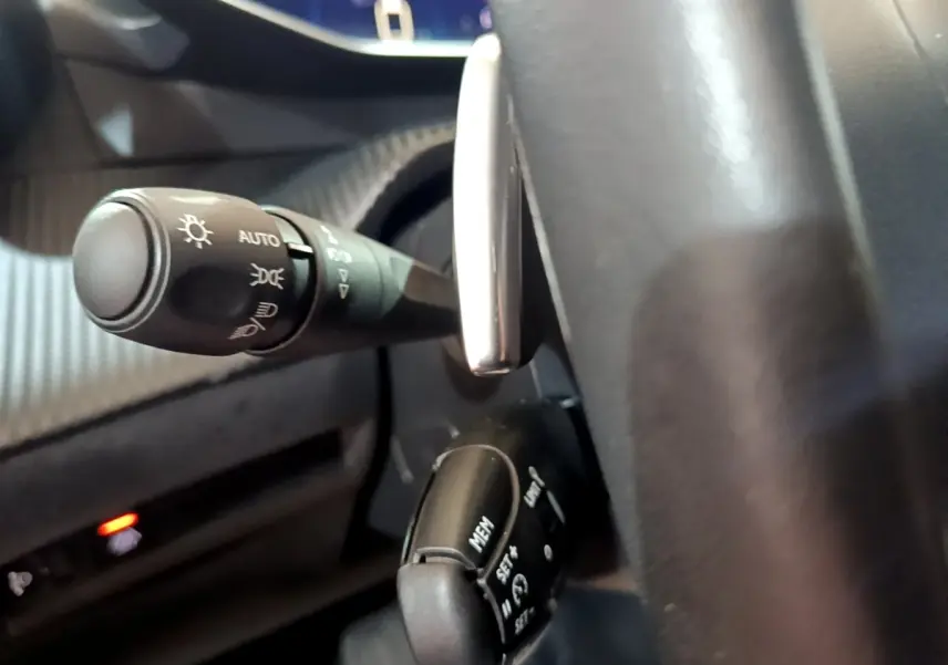 Gros plan sur le commodo des phares et le régulateur de vitesse derrière le volant cuir d’un Peugeot 2008 noir.