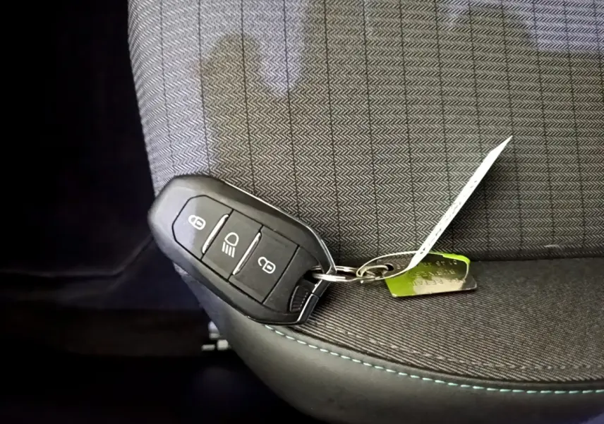 Clé de contact noire posée sur un siège tissu gris à surpiqûres bleues dans l'habitacle d'une Peugeot 2008 noire.