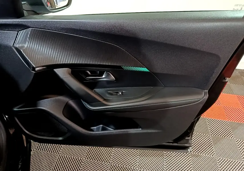 Vue intérieure du panneau de porte avant gauche noir du Peugeot 2008 2021 avec insert effet carbone et bouton de lève-vitre.