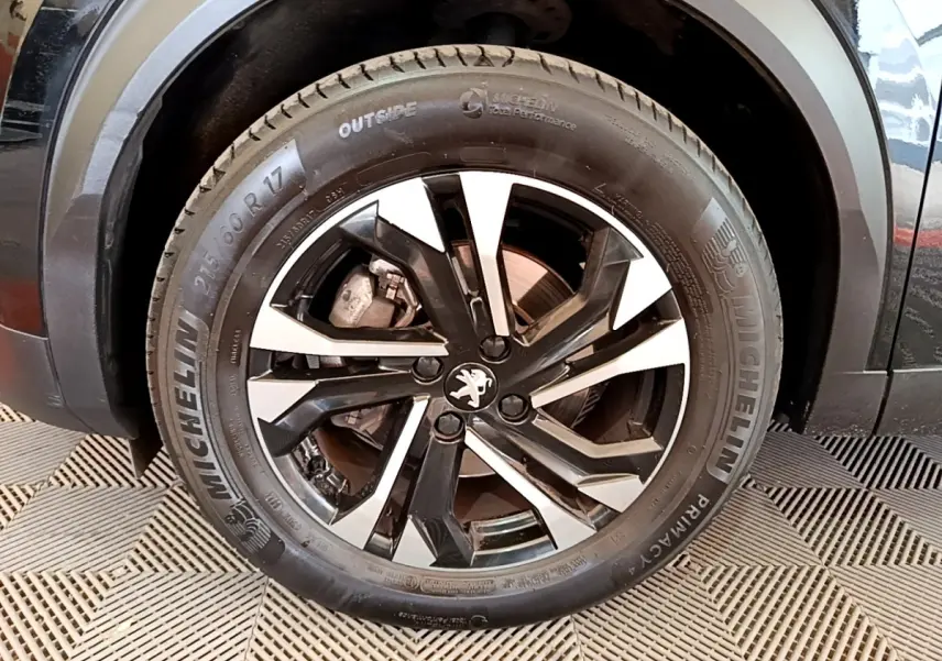 Gros plan sur la roue avant gauche noire d’un Peugeot 2008 2021 avec jante alliage bicolore et pneu Michelin.