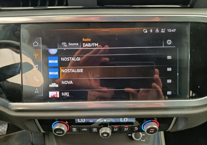 Écran tactile central de l’Audi Q3 Sportback 35 TDI 2023 affichant les stations radio DAB/FM, avec commandes climatisation en dessous.