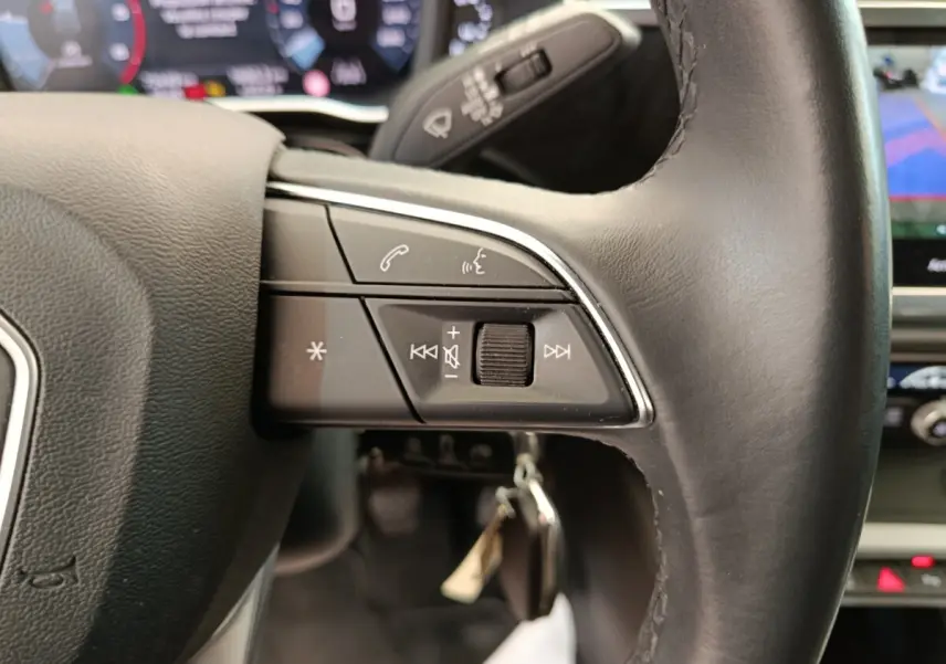 Gros plan sur le volant cuir noir de l'Audi Q3 Sportback 35 TDI, avec commandes multifonctions et tableau de bord numérique flou.