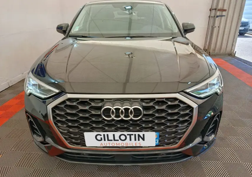 Vue avant d’un Audi Q3 Sportback noir 2023 avec calandre hexagonale et phares LED allumés dans un garage.