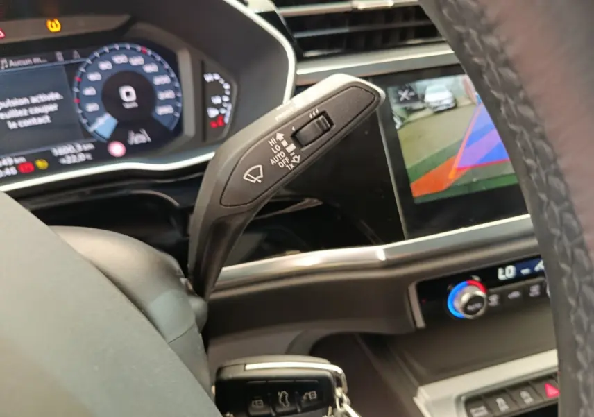 Vue intérieure rapprochée du volant et du commodo d’essuie-glace d’un Audi Q3 Sportback noir avec affichage numérique et écran multimédia.