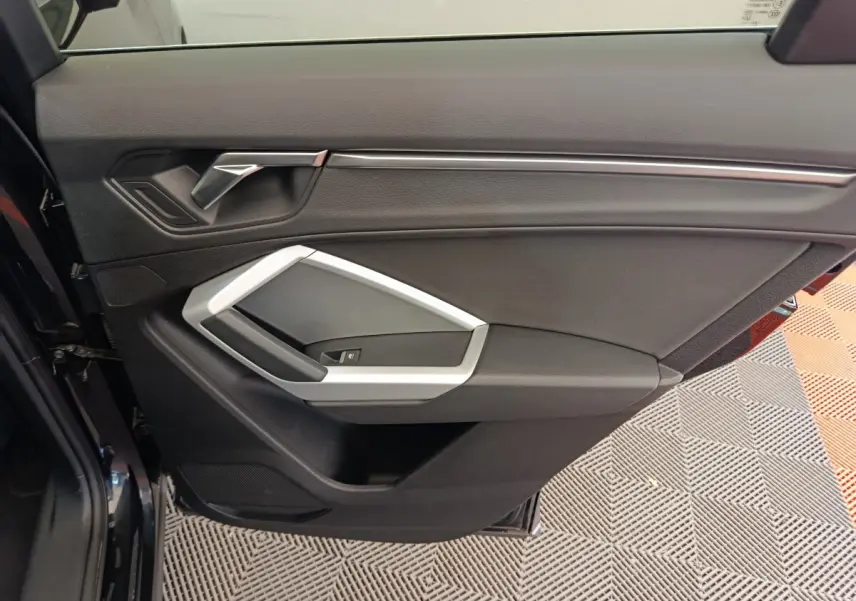 Vue rapprochée de la porte avant gauche noire de l’Audi Q3 Sportback 35 TDI avec poignée argentée et garniture intérieure noire.