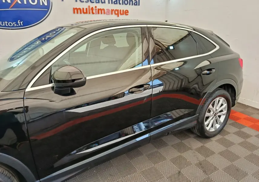 Vue de profil côté gauche d'un Audi Q3 Sportback noir brillant dans un showroom intérieur.