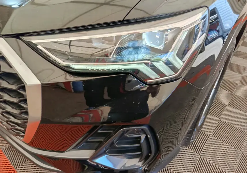 Gros plan sur le phare avant droit noir brillant de l'Audi Q3 Sportback 35 TDI 2023 avec calandre hexagonale.