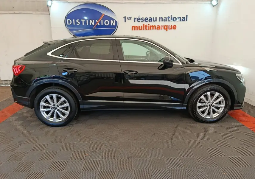Vue latérale droite d'un Audi Q3 Sportback noir 2023, avec jantes alliage et lignes épurées sous un éclairage intérieur.