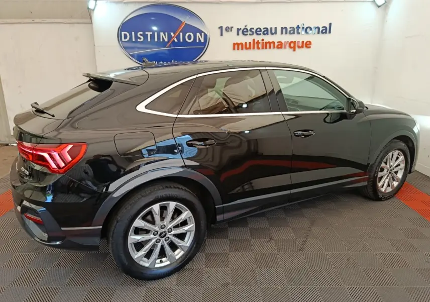 Audi Q3 Sportback noir vue 3/4 arrière droit, avec feux LED et jantes alliage visibles en intérieur showroom.