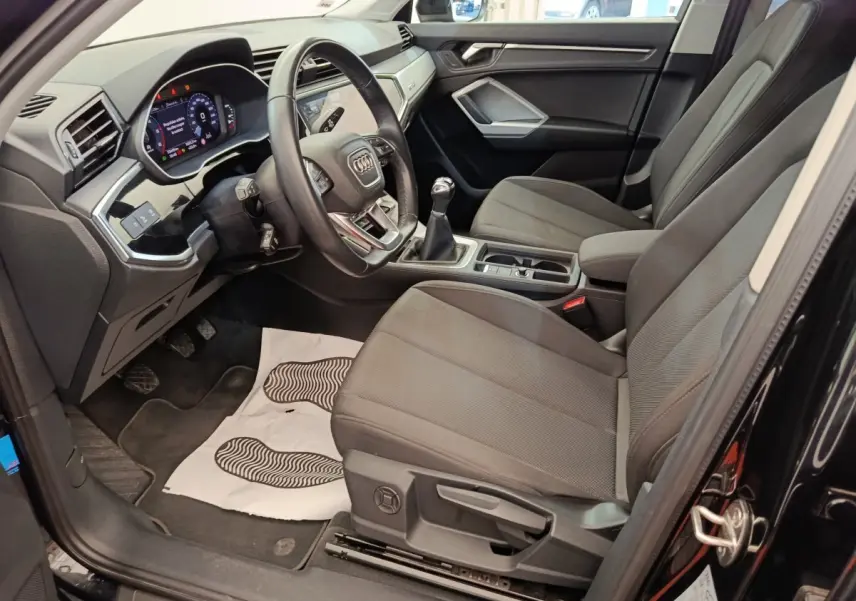 Intérieur avant droit de l’Audi Q3 Sportback noir 2023, volant cuir multifonctions et boîte manuelle visible.