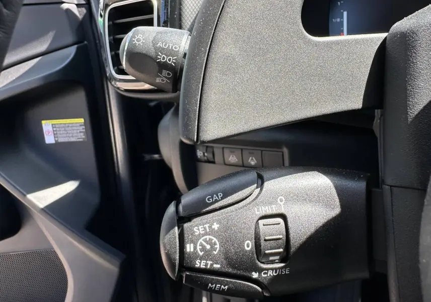 Gros plan sur la commande de régulateur de vitesse à gauche du volant dans l’habitacle noir du Citroën C5 Aircross gris Platinium.