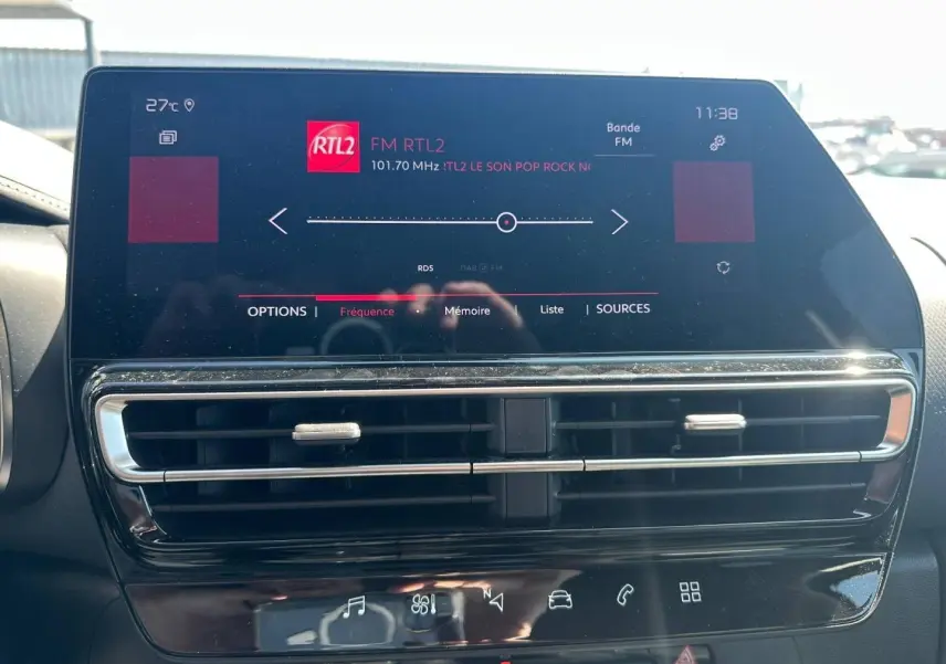 Écran tactile central allumé avec radio FM RTL2, entouré de sorties d'air et commandes tactiles noires brillantes.