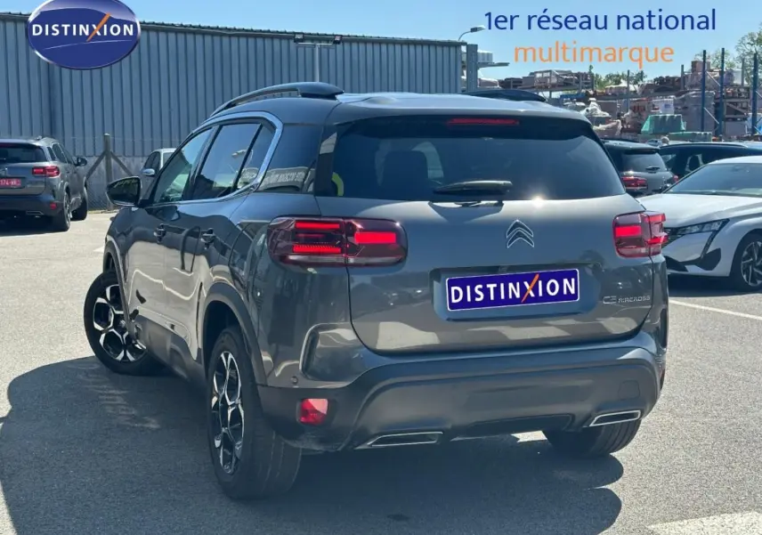 Vue 3/4 arrière droite d'un Citroën C5 Aircross gris Platinium avec barres de toit et feux arrière LED allumés.