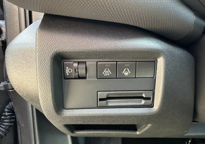 Vue rapprochée des commandes de réglage des phares et d'assistance à la conduite sur le côté gauche du tableau de bord gris du Citroën C5 Aircross.