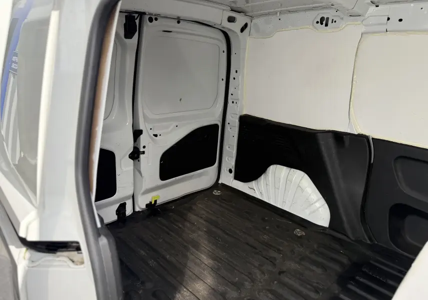 Intérieur arrière du Peugeot Partner blanc 2021, vue depuis la porte latérale ouverte, espace de chargement vide avec revêtement noir.