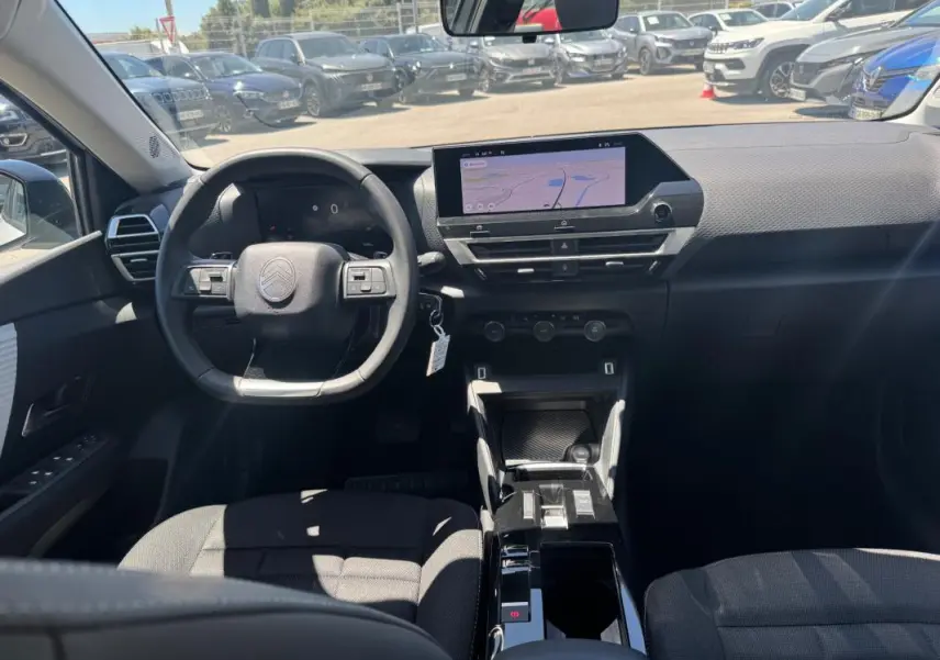 Vue intérieure avant du Citroën C4 hybride blanc 2025, avec volant cuir, écran tactile et console centrale moderne.