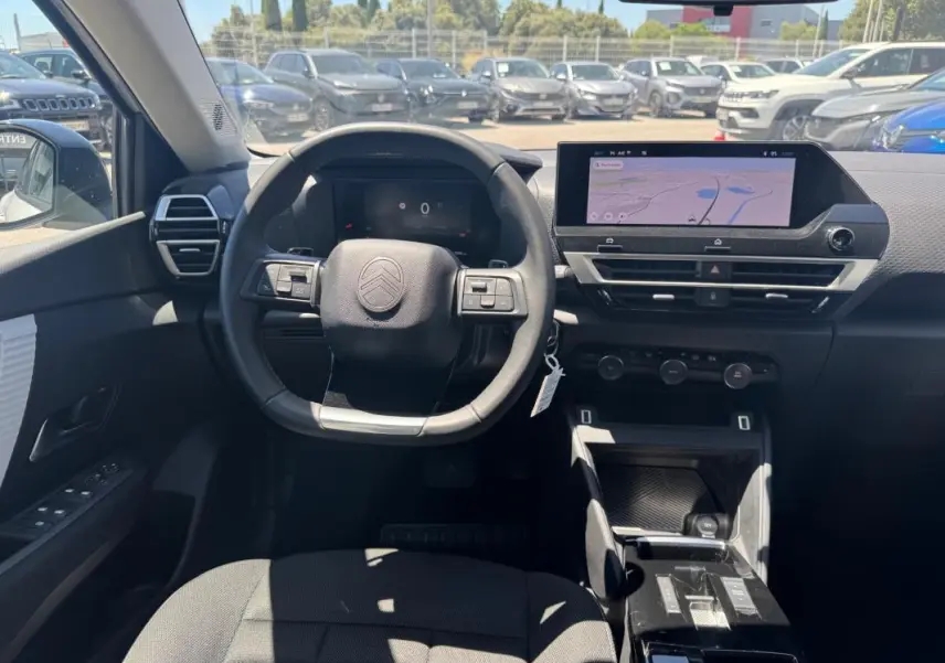 Vue intérieure avant du poste de conduite de la Citroën C4 blanche, avec volant cuir et écran tactile central affichant la navigation.