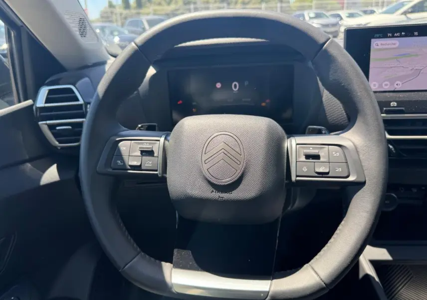 Vue rapprochée du volant cuir noir de la Citroën C4 hybride 2025 avec commandes intégrées et tableau de bord numérique.