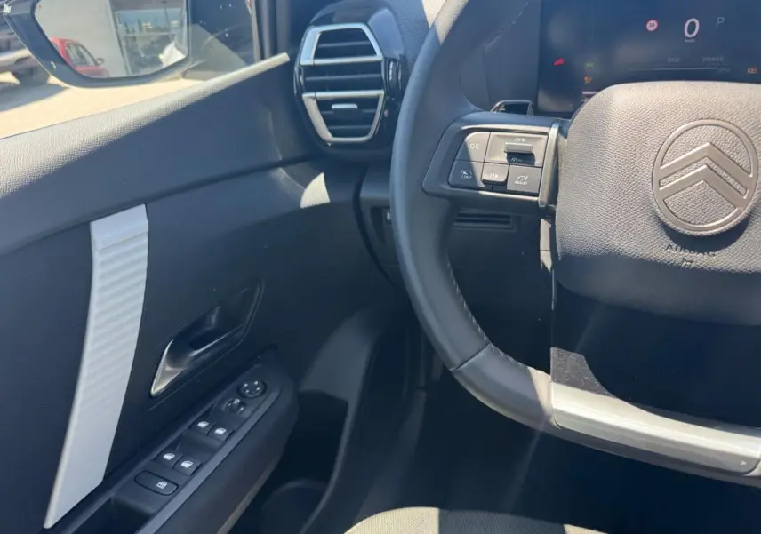 Vue intérieure côté conducteur du Citroën C4 hybride blanc 2025, volant cuir et commandes au volant visibles.