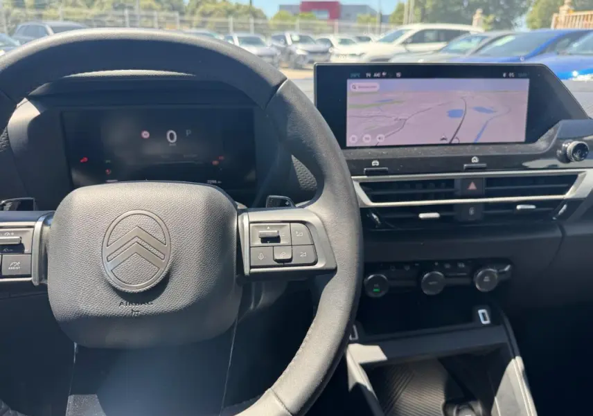 Vue intérieure centrée sur le volant cuir et l'écran tactile du tableau de bord du Citroën C4 blanc hybride 2025.
