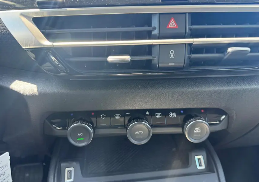 Gros plan sur la console centrale de la Citroën C4 hybride blanche, montrant les commandes de climatisation automatique et la prise USB.