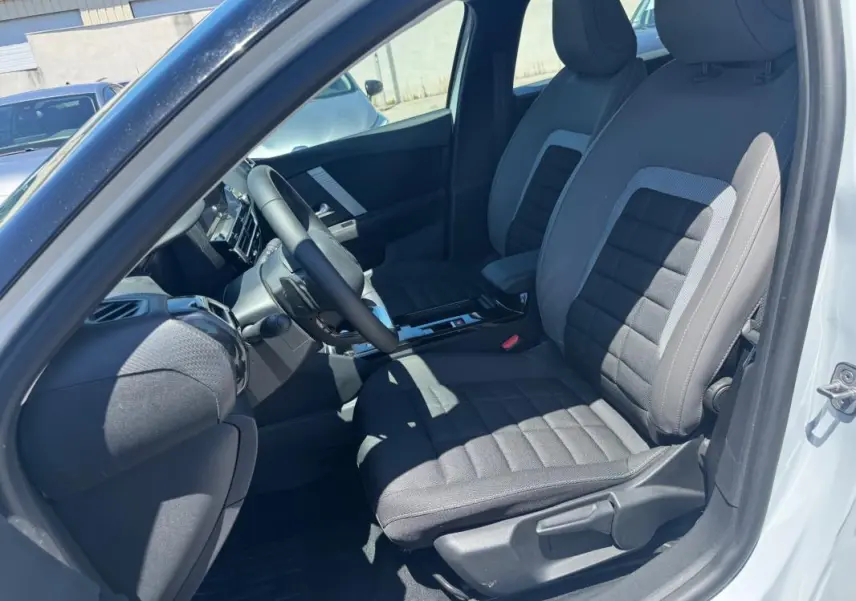 Vue intérieure côté conducteur de la Citroën C4 hybride blanche 2025, sièges tissu gris et volant cuir.
