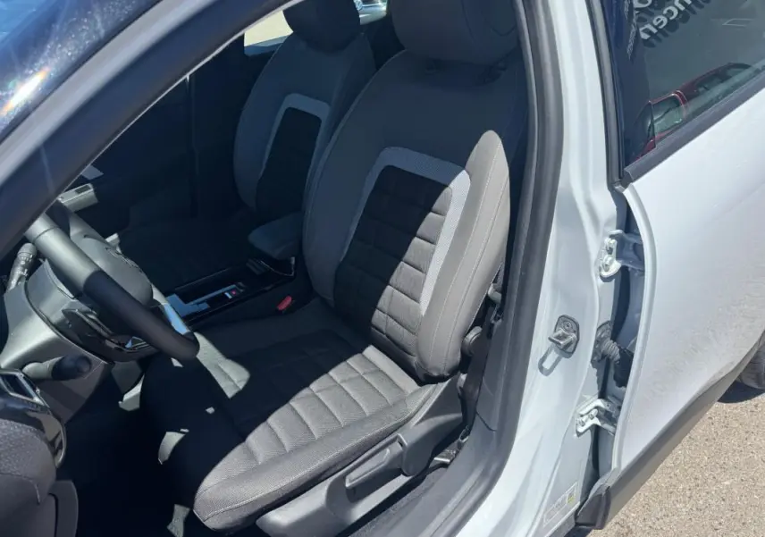 Vue intérieure côté conducteur de la Citroën C4 blanche 2025, montrant le siège avant en tissu gris et noir.