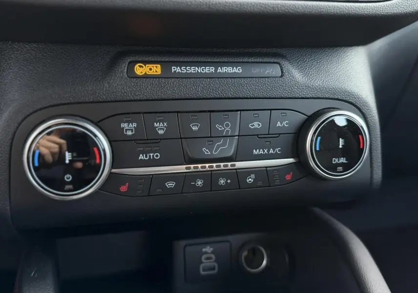 Gros plan sur la console de climatisation du Ford Kuga noir, avec commandes chauffantes et affichage airbag passager.