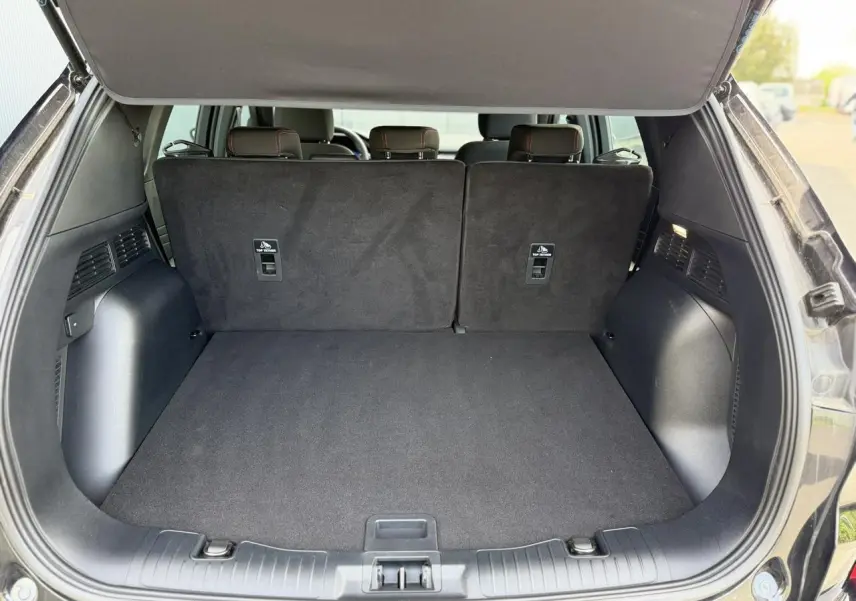 Coffre ouvert d’un Ford Kuga noir Agathe, vue arrière montrant l’espace de chargement et les dossiers de sièges arrière.