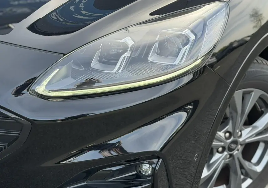 Gros plan sur le phare avant droit et la roue alliage 18 pouces du Ford Kuga noir Agathe ST-Line 2023.