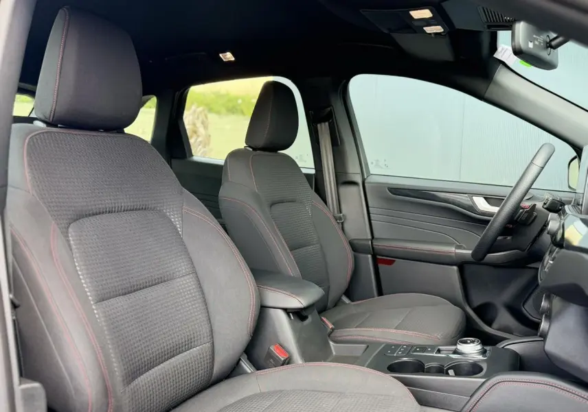 Vue intérieure côté conducteur du Ford Kuga 2023 avec sièges tissu noirs et surpiqûres rouges, volant ST-Line à méplat.