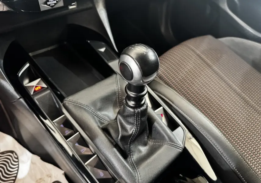 Gros plan sur le levier de vitesse manuel en cuir noir dans l’habitacle du DS3 Crossback gris foncé, siège tissu à motifs visible.