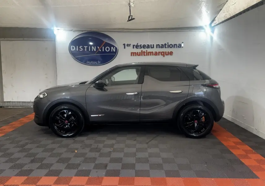 Vue de profil côté gauche d'un DS3 Crossback gris foncé avec jantes noires brillantes dans un showroom.