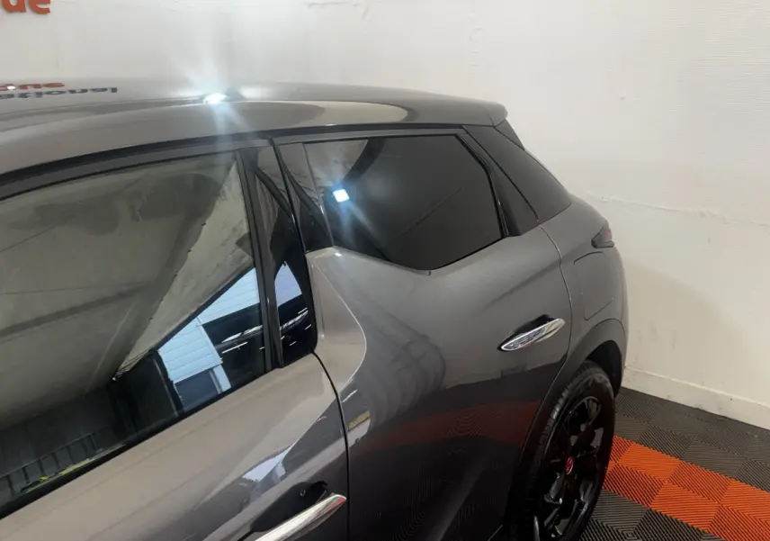 Vue côté droit arrière du DS3 Crossback gris foncé, mettant en valeur la poignée de porte chromée et les jantes noires.
