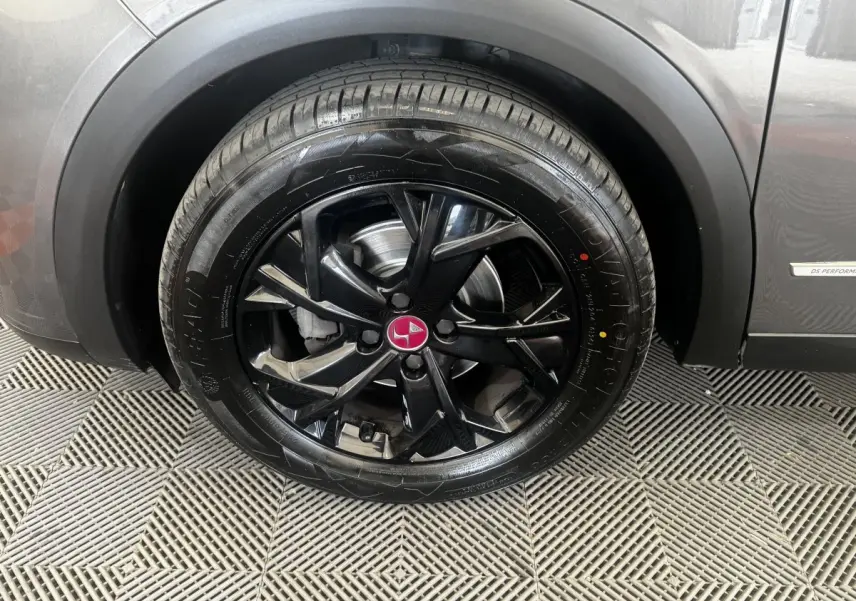 Gros plan sur la roue avant droite noire brillante d’un DS3 Crossback gris foncé avec logo rouge au centre.