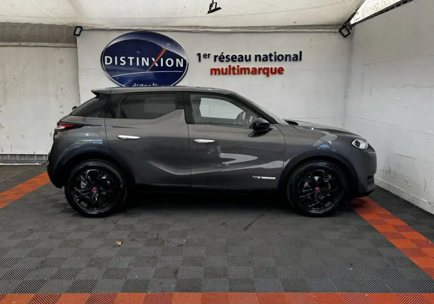 Vue de profil côté gauche d’un DS3 Crossback gris foncé avec jantes noires et toit noir dans un showroom.