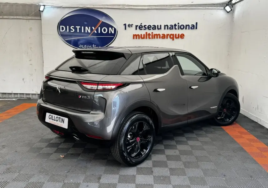 Vue 3/4 arrière droite d'un DS3 Crossback gris foncé avec jantes noires et toit noir dans un showroom.