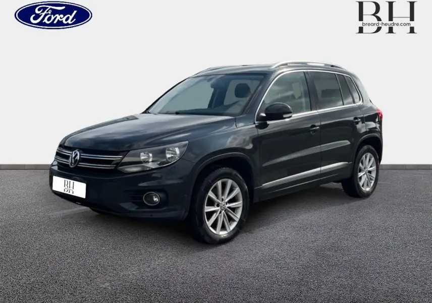 Volkswagen Tiguan gris poivre vu en 3/4 avant droit avec jantes alu et barres de toit visibles.