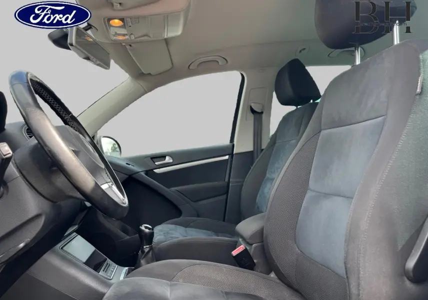 Vue intérieure côté conducteur du Volkswagen Tiguan 2014, sièges sport en tissu gris avec volant cuir.