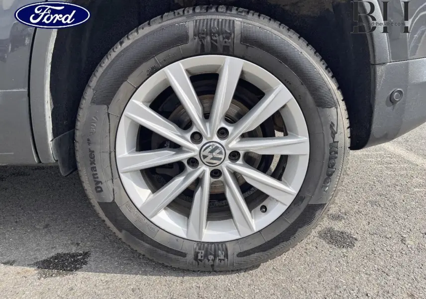 Gros plan sur la jante alu argentée avec logo Volkswagen, montée sur un pneu noir, partie arrière droite du Tiguan gris poivre.