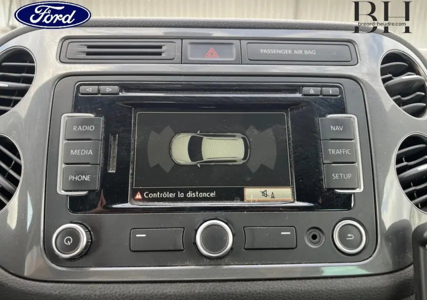 Tableau de bord avec écran tactile affichant l'aide au stationnement d'un Volkswagen Tiguan gris poivre, vue de face rapprochée.