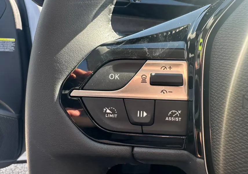 Gros plan sur les commandes de régulateur de vitesse au volant noir du Peugeot 308 SW hybride blanc Okénite.