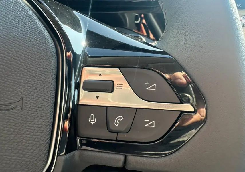 Gros plan sur les commandes multifonctions noires et argentées du volant d’une Peugeot 308 SW hybride blanche.