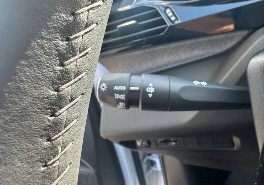 Gros plan sur la commande des phares et clignotants à gauche du volant dans l'habitacle d'une Peugeot 308 SW blanche.